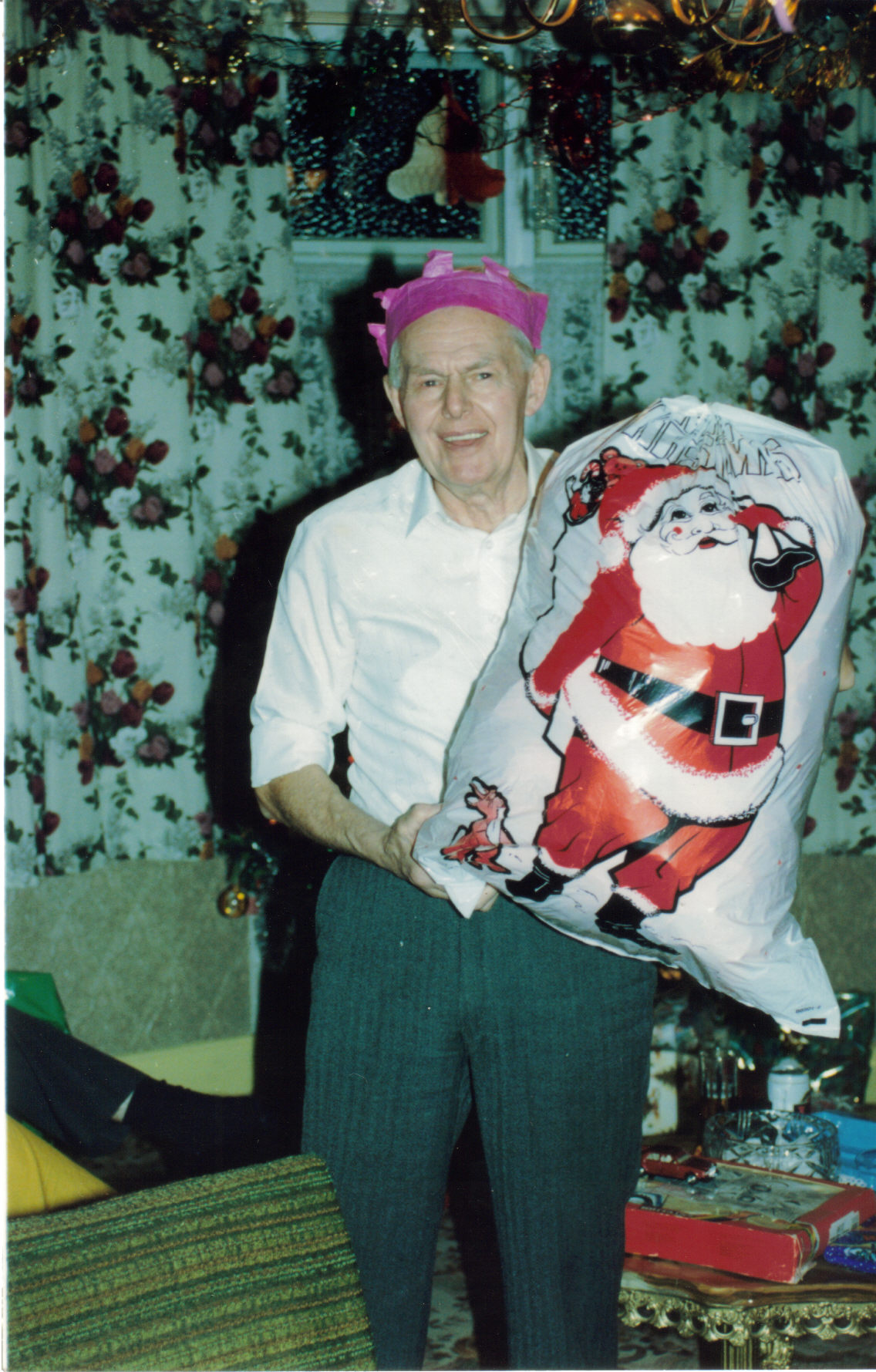 My elderly grandad smiling as he holds up a large bulging white sack with a picture of Santa on the front.