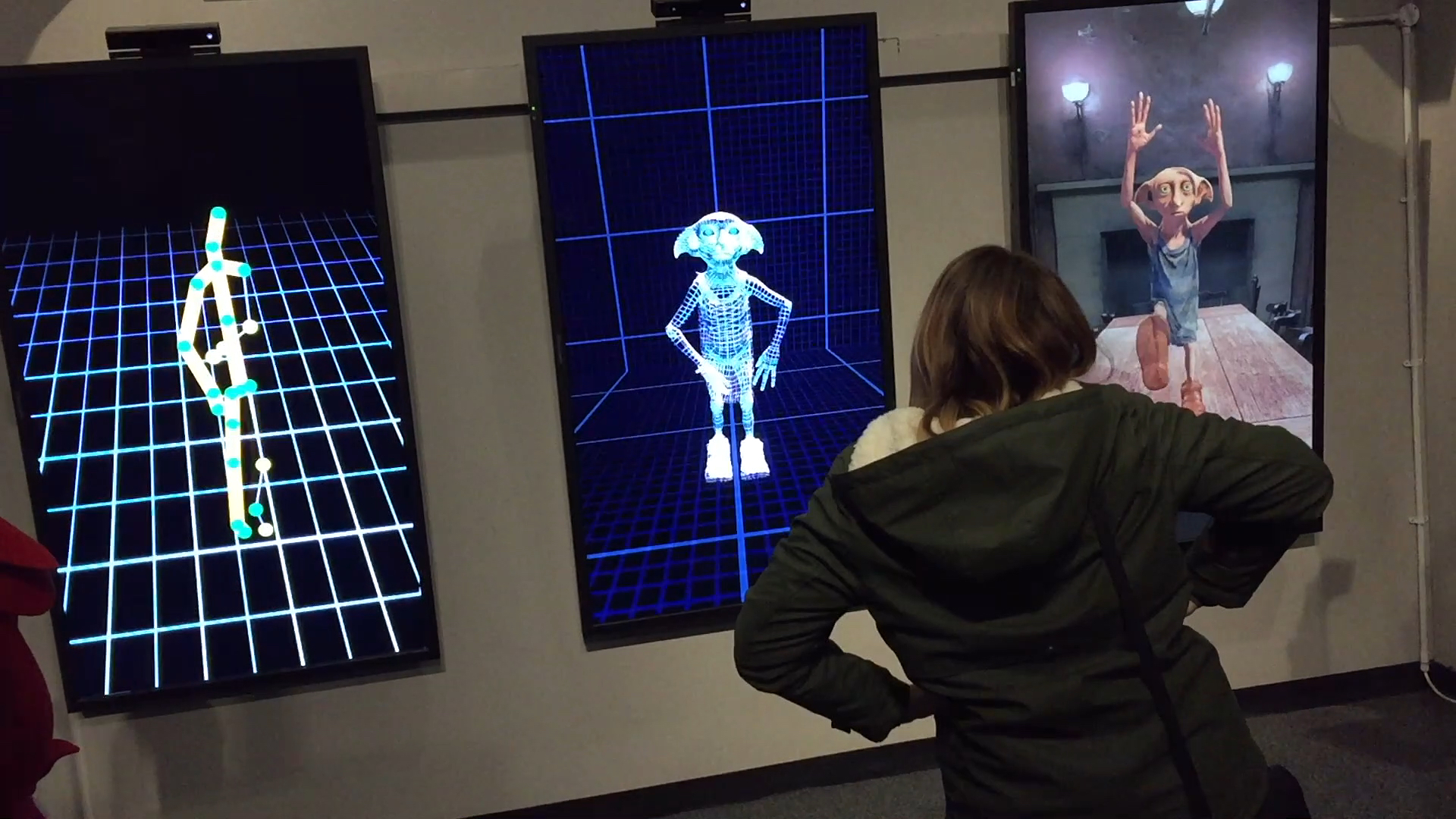 3 vertical screens - one showing a stick figure, one showing a skeleton of Dobby, and one showing a fully rendered version of Dobby. In each case, the animation on the screen is matching the movements of the people standing in front of it.