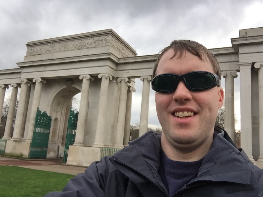 Selfie of Glen in front of the huge gateway to Hyde Park, consisting of 3 tall archways separated by many stone columns.