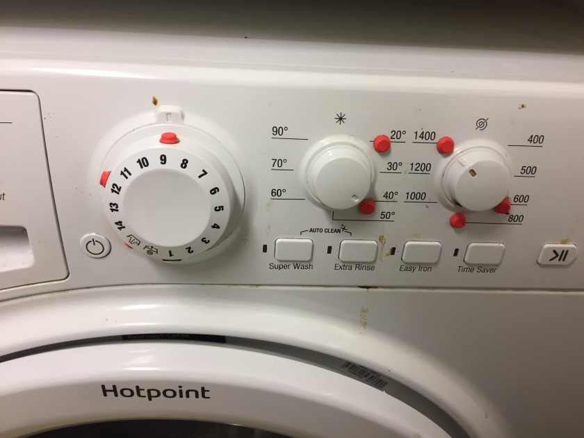 Close-up view of 3 dials, 1 big and 2 small, on a washing machine, with red tactile dots called bumpons stuck on a few of the numbers to indicate their positions.