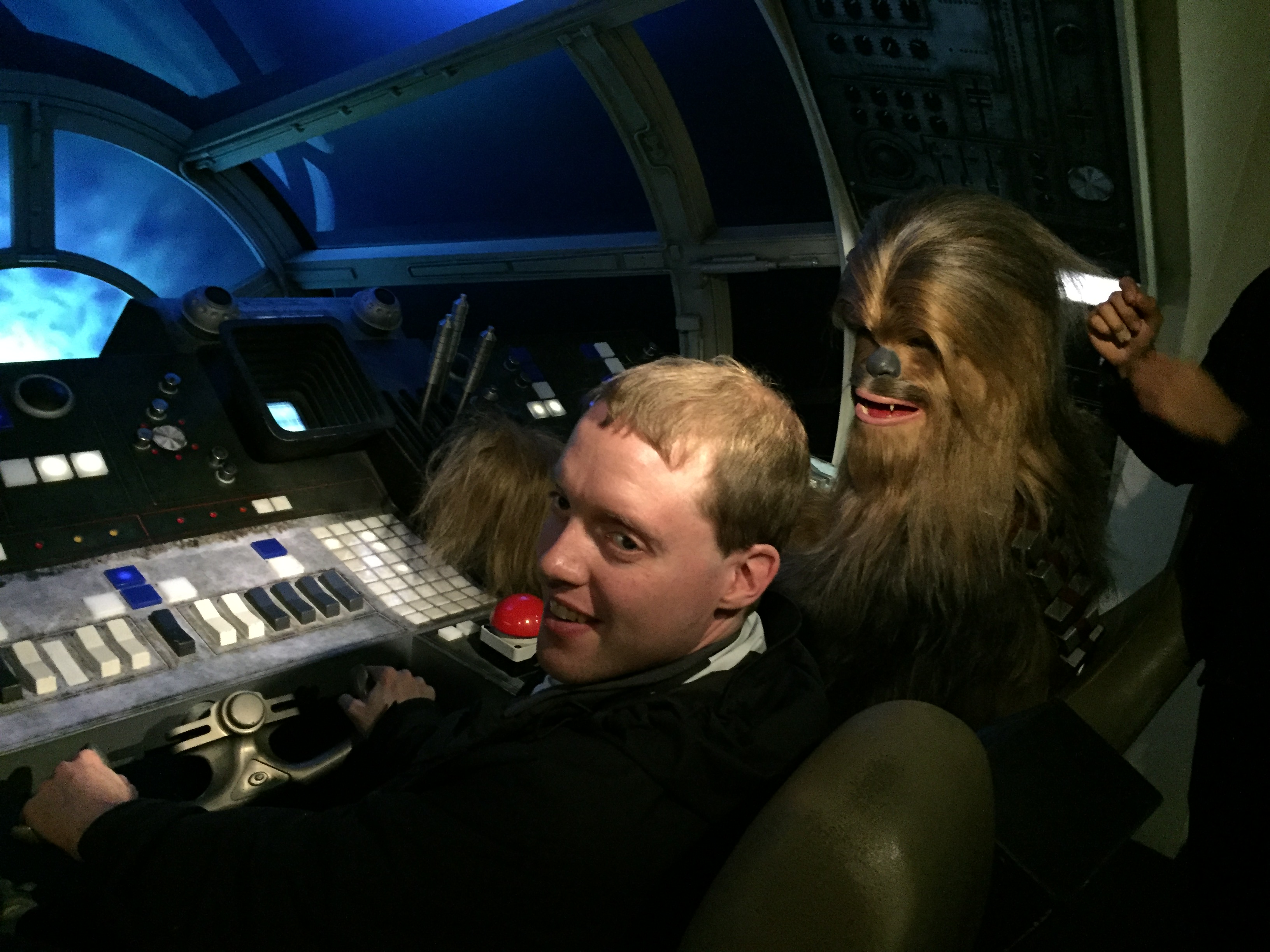 Glen sitting in the driving seat of the Millennium Falcon from Star Wars, with a waxwork of Chewbacca, a large and very hairy creature, in the seat next to him.