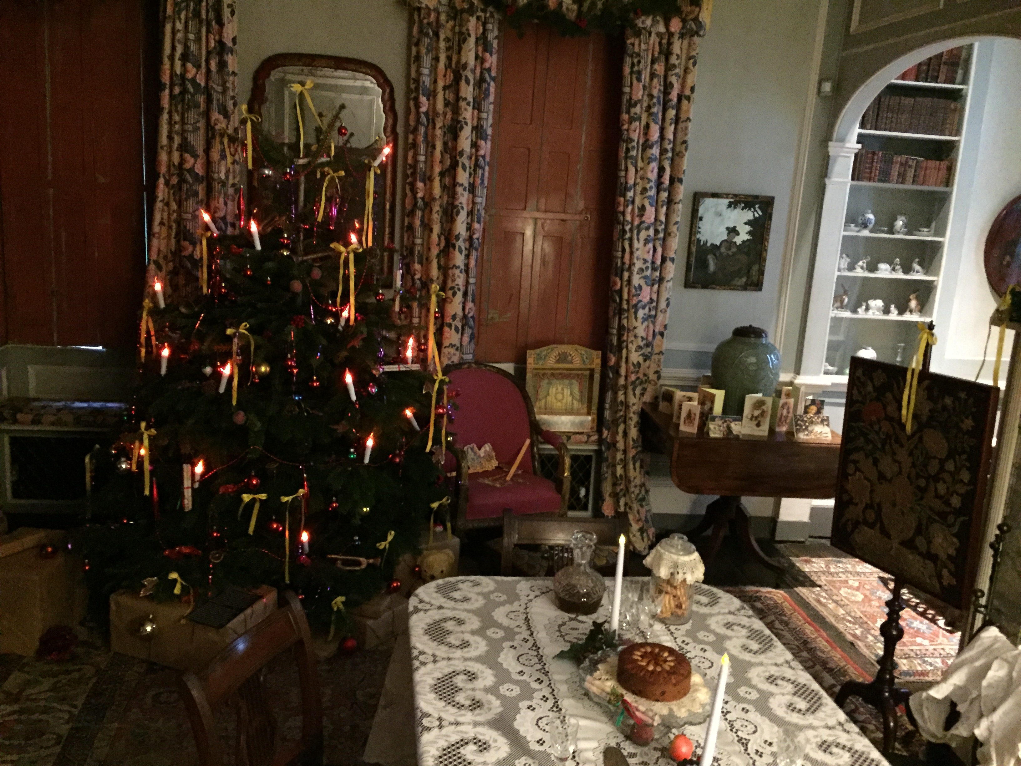 Victorian Christmas room at Fenton House, with a Christmas tree adorned with lights that look like candles, a small dining table with a couple of candles and some items of food on it, and Christmas cards on a desk.