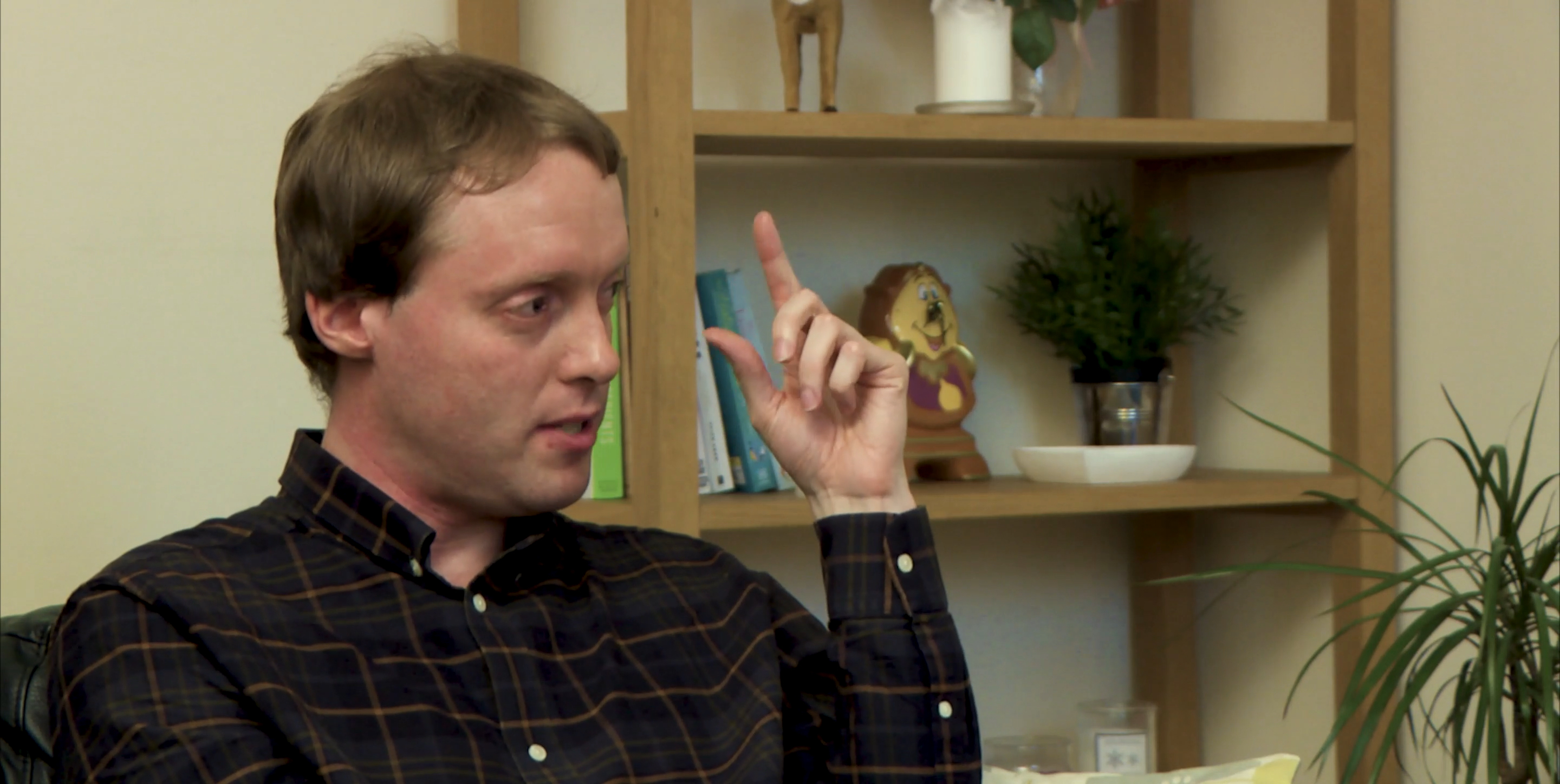 Close-up of Glen gesturing with his fingers near his eye, during his interview in a living room.