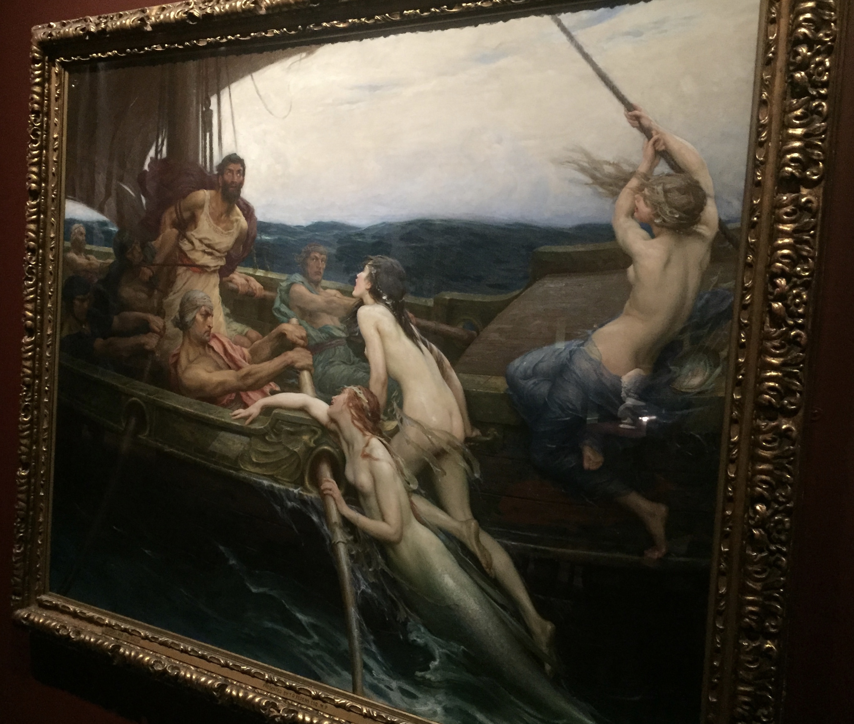 Painting entitled Ulysses and the Sirens. It shows Ulysses, a tall bearded man, tied to the mast of a ship being rowed by a group of men. His eyes are wide open, transfixed by the beauty of the three naked mermaids who are trying to climb on to the boat to reach him.