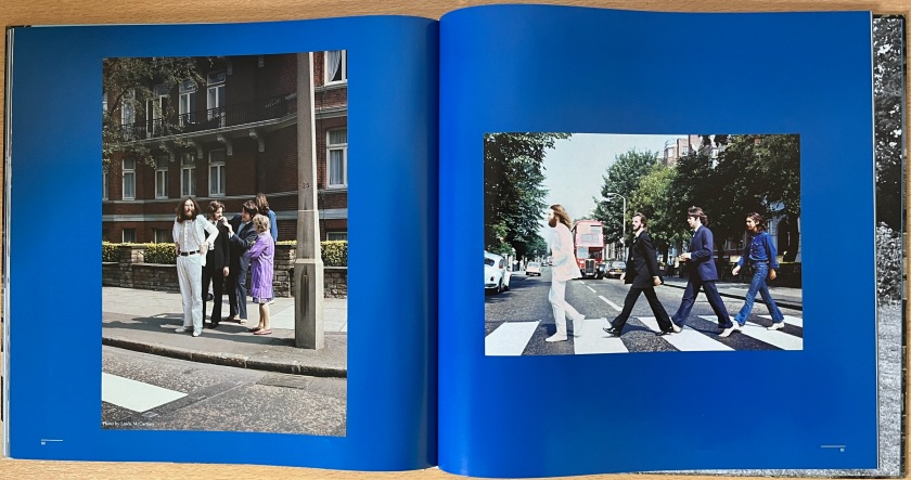 Double-page spread from the Abbey Road box set book, showing 2 images from the Abbey Road zebra crossing photo shoot. One shows the band standing on the pavement talking a lady, while the other shows the band members striding over the crossing from right to left, the opposite direction to the final album cover image.