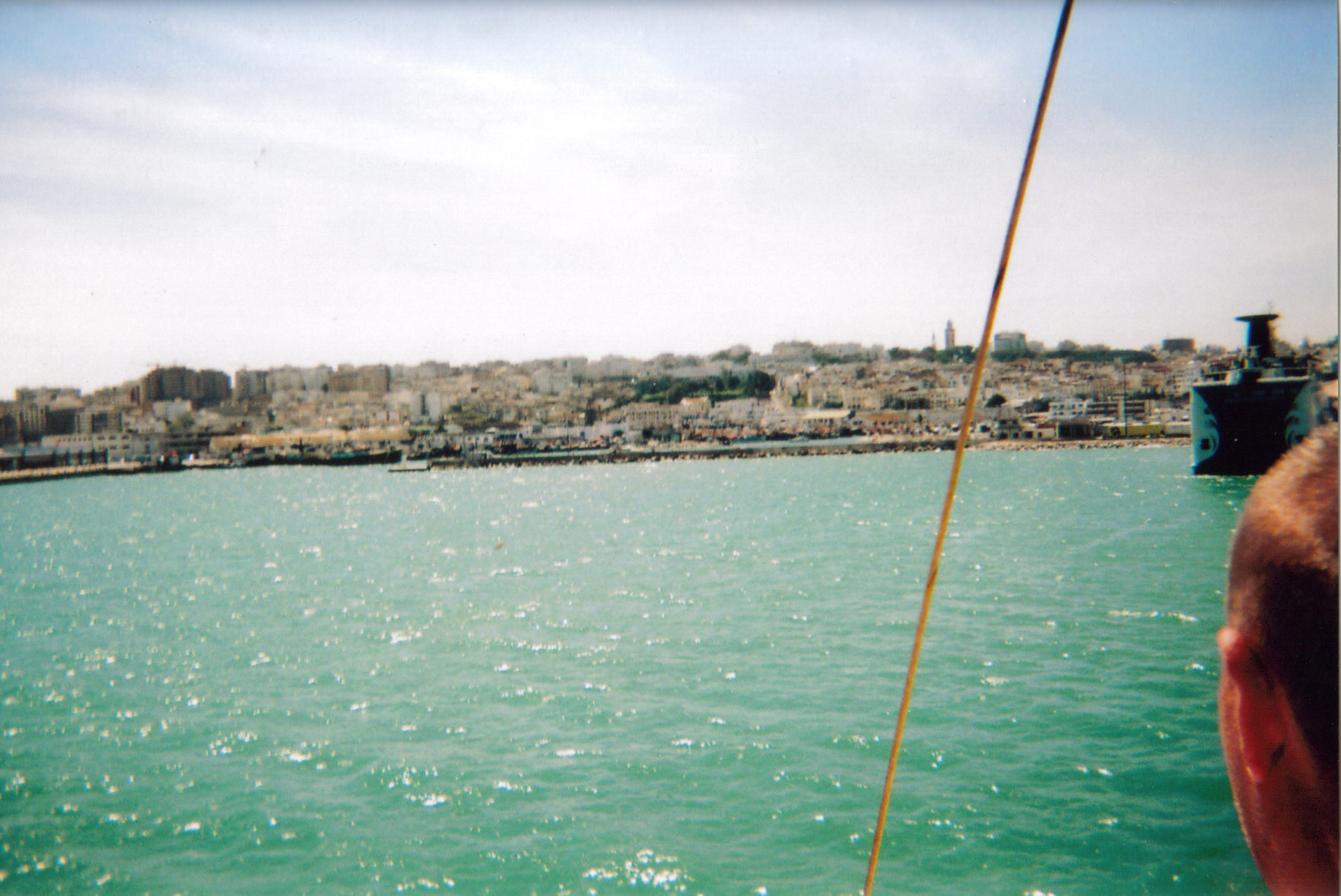 View from a boat towards the shore of Tangier in Morocco, with lots of buildings visible on the hilly landscape.