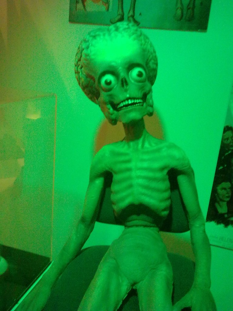 A small green alien skeleton with a grinning mouth and bulging eyes.