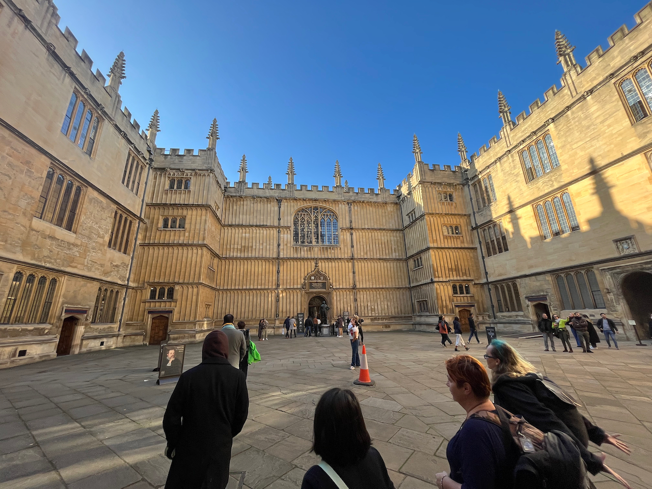 The large quadrangle of the Bodleian Library. The section ahead has 4 floors, with a large ornate arched window in the centre of the top 2 floors, while the left and right sections of the building have 3 levels.