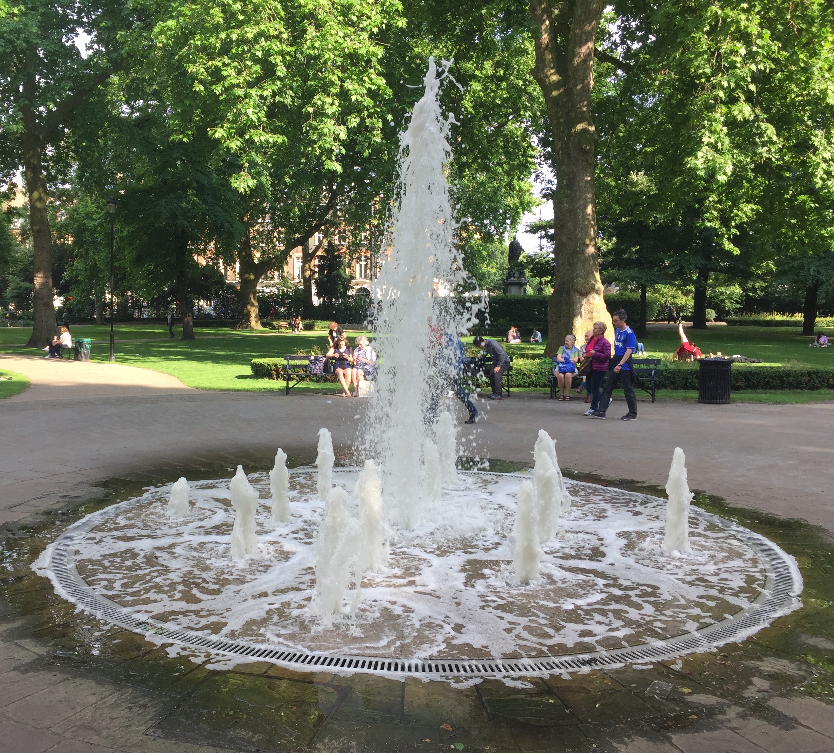 A circular paved area in Russell Square containing a tall fountain spurting out of the centre, and lots of smaller fountains all around it.