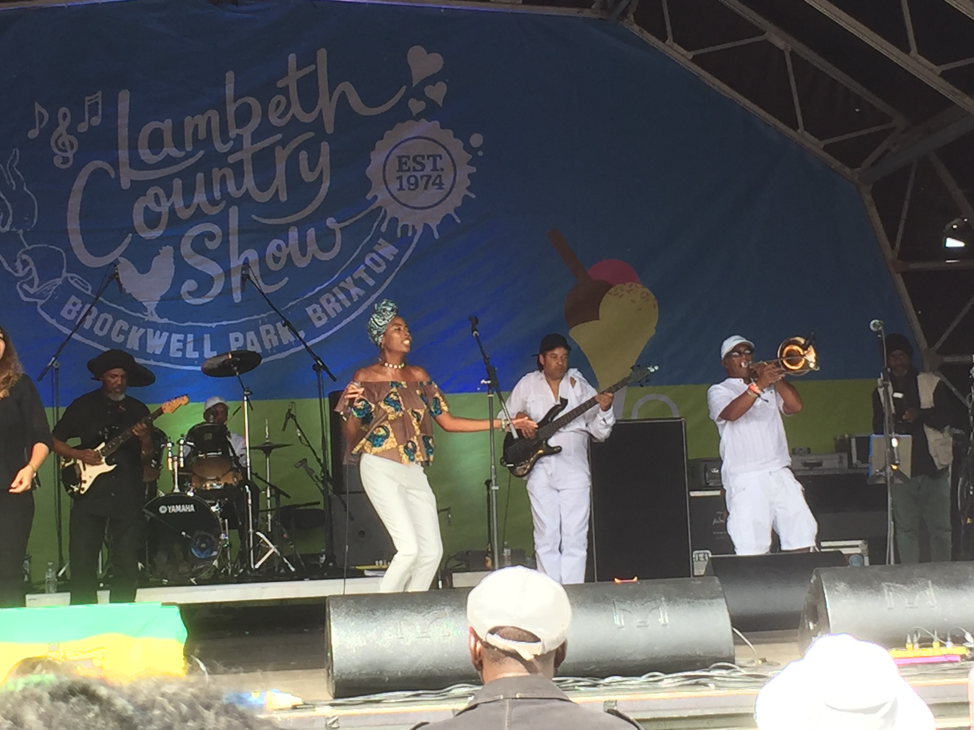 Teshay Makeda singing on stage at the Lambeth Country Show, accompanied by a couple of guitarists, a trumpet player and a drummer.
