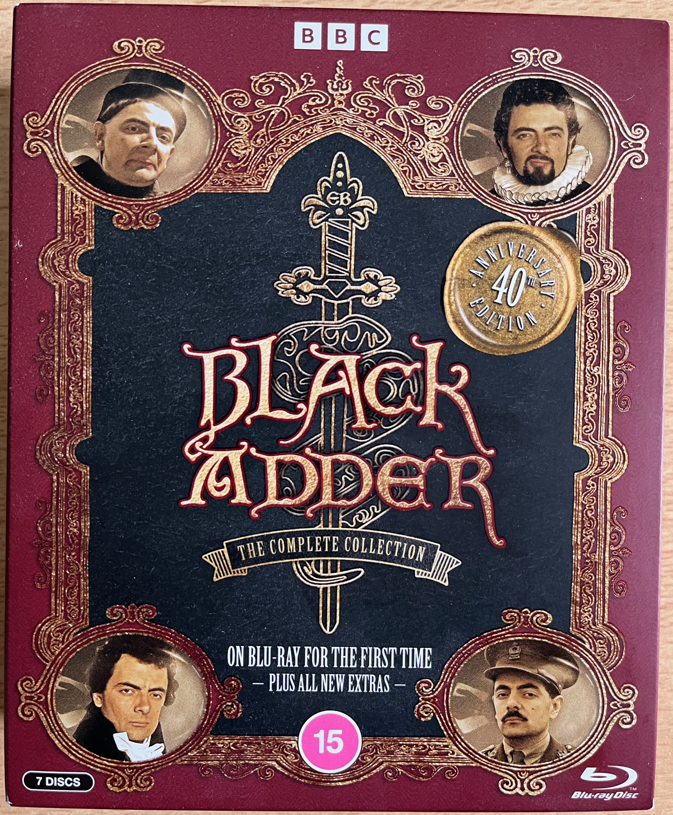 Front cover of Blackadder The Complete Collection, 40th Anniversary Edition, with small text at the bottom saying that it's on Blu-ray for the first time, plus all new extras. An ornate gold border has a circle in each corner, with a photo of Blackadder from each of the 4 series.